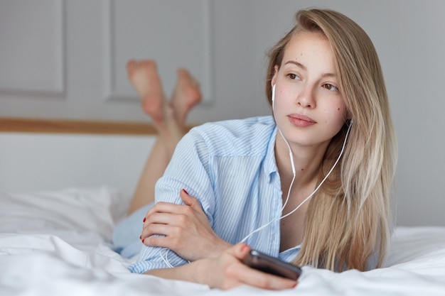 Beautiful young woman relaxing in bed and listening to music