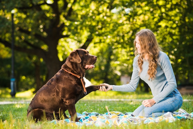 Beautiful young woman shaking dog's paw in garden