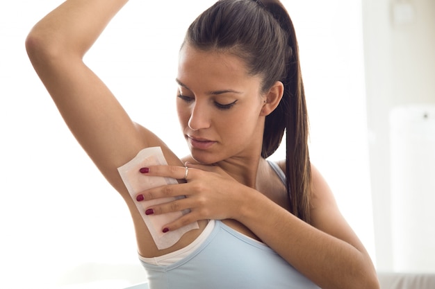 Beautiful young woman shaving her armpit with wax in the bathroom.