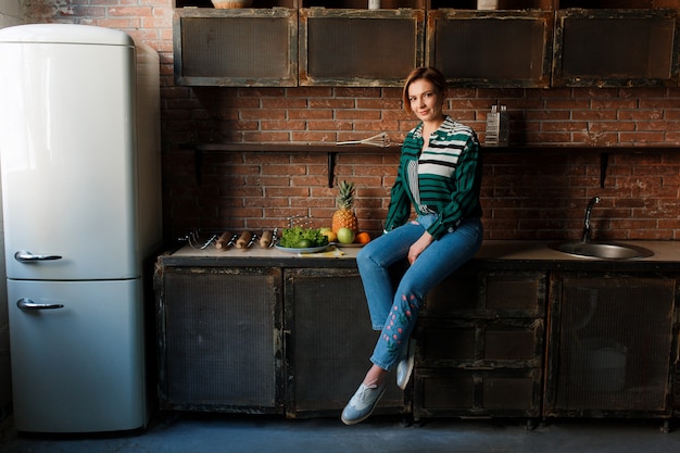 Free Photo beautiful young woman short haircut sitting on kitchen table. 