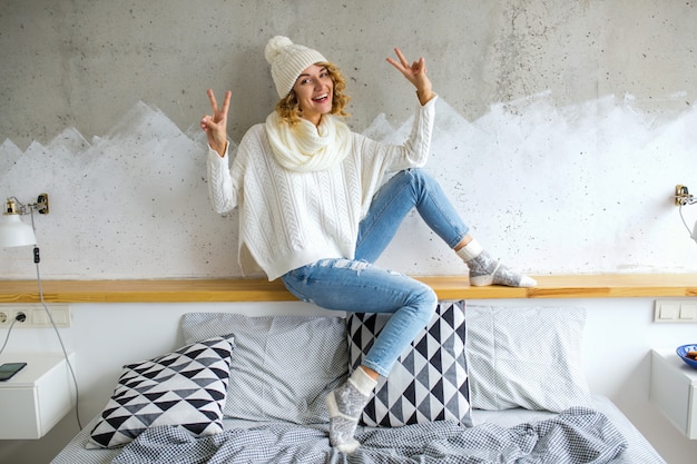 Free photo beautiful young woman sitting in bedroom against wall wearing white sweater