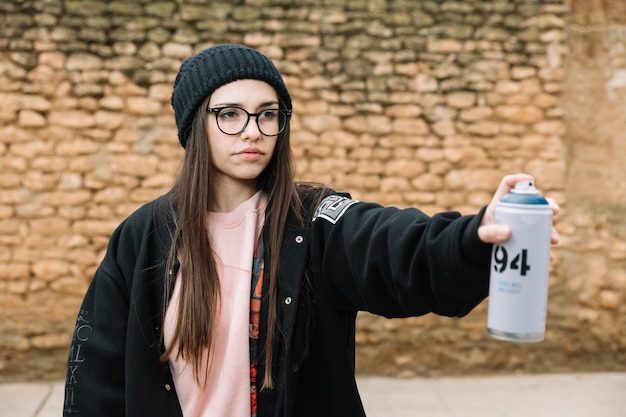 Free photo beautiful young woman spraying aerosol can standing in front of stone wall