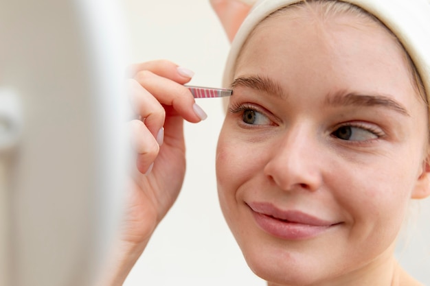 Free photo beautiful young woman using tweezers on her brows