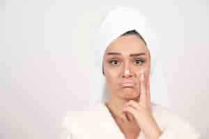 Free photo beautiful young woman in a white bathrobe posing on a white wall