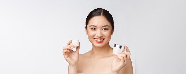 Beautiful young woman on white isolated background holding cosmetic face cream asian