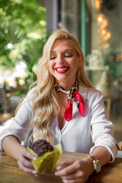 Beautiful young woman with long blonde hair holding delicious chocolate muffin in hand