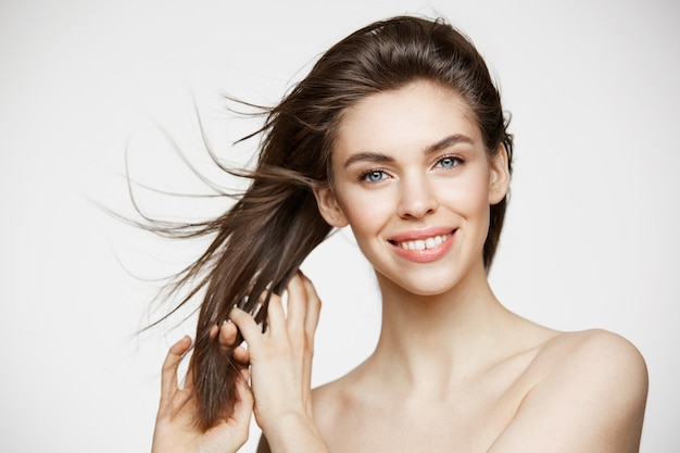 Free photo beautiful young woman with perfect clean skin smiling touching hair over white wall. facial treatment.