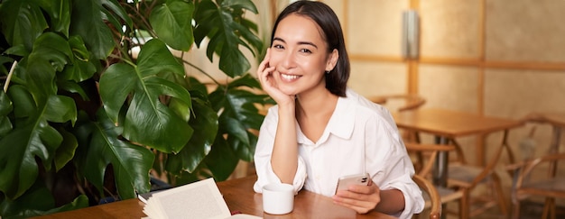 Free photo beautiful young woman with smartphone drinking coffee in cafe and smiling relaxing with favorite