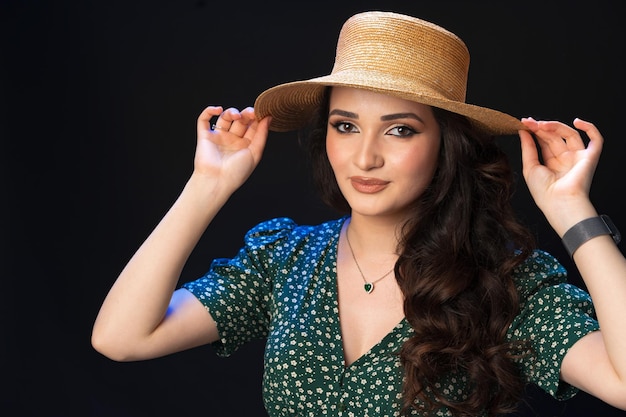 Beautiful young woman with straw hat posing against black background