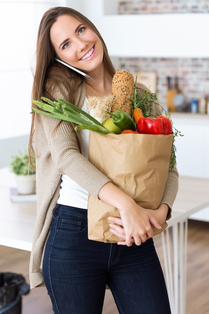 Beautiful young woman with vegetables in grocery bag at home.