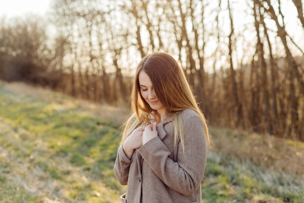 Beautiful young woman in wool coat on the forest at sunset