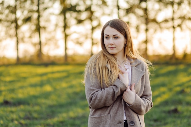 Beautiful young woman in wool coat on the forest at sunset