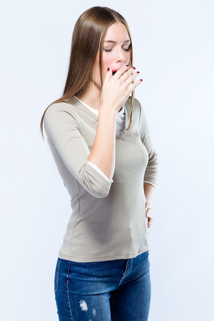 Beautiful young woman yawning over white background.