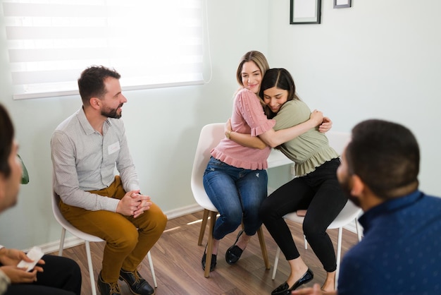 Beautiful young women hugging and smiling after finishing a group therapy session. Feeling happy to overcome my mental health problems together