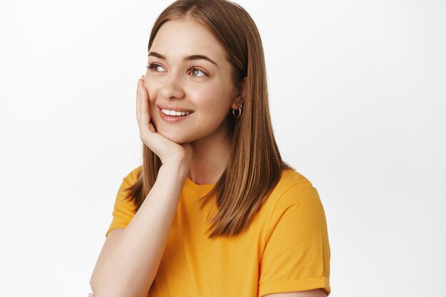 Beauty. Close up portrait of dreamy happy woman, smiling looking aside with thoughtful daydreaming face, touching clean glowing skin, standing over white background.