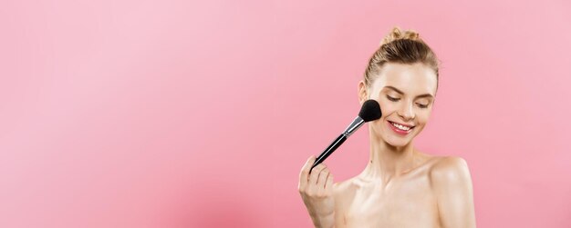 Beauty Concept Closeup Beautiful caucasian woman applying makeup with Cosmetic Powder Brush Perfect Skin Isolated on pink background and copy space