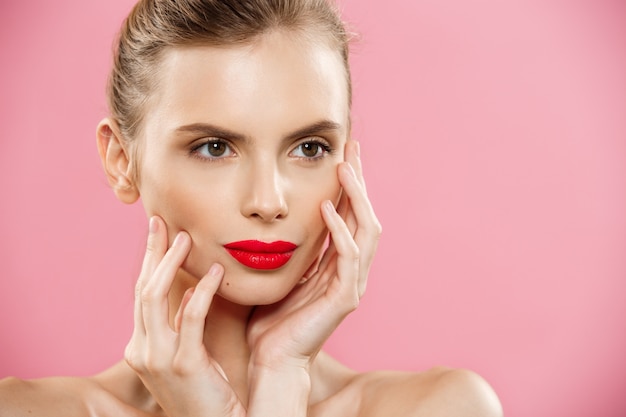 Free photo beauty concept - woman applying red lipstick with pink studio background. beautiful girl makes makeup.