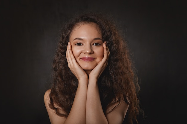 Beauty, joy and happiness concept. Portrait of charming adorable young woman resting chin on her hands