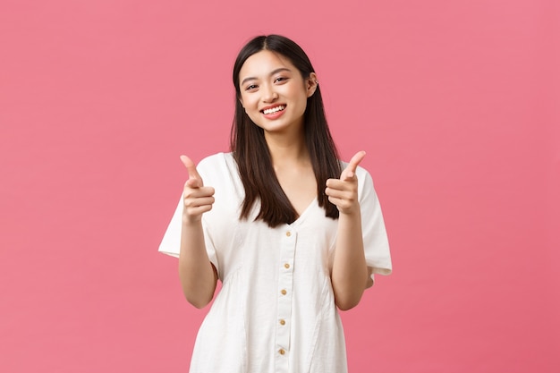 Beauty, people emotions and summer leisure and vacation concept. Cheerful silly korean girl in white dress, showing thumbs-up and smiling, smiling pleased, satisfied with product, recommend it