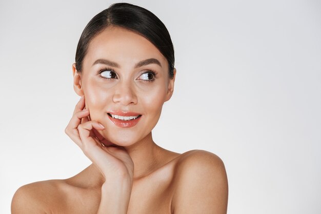 Beauty picture of gentle woman with brown hair looking aside and holding hand at her perfect face, isolated over white