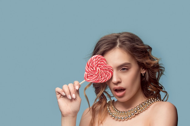 Free photo beauty portrait of a cute girl in act to eat a candy over blue studio