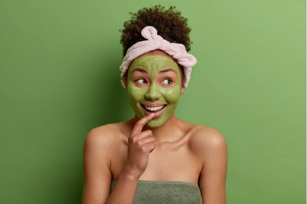 Beauty portrait of happy female model applies green nourishing mask on face