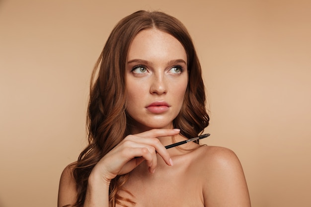 Free photo beauty portrait of mystery ginger woman with long hair looking away while holding cosmetics brush