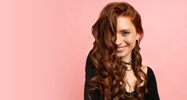 beauty portrait of red head woman posing over pink wall. Wavy hairs. Perfect smile.