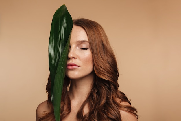 Free photo beauty portrait of sensual ginger woman with long hair posing with green leaf