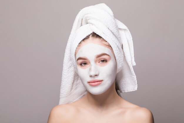 Beauty portrait of woman in towel on head with white nourishing mask or creme on face, white wall isolated. Skincare cleansing eco organic cosmetic spa relax concept