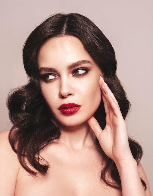 Beauty portrait of young brunette woman with evening makeup and perfect clean skin Sexy model with curly hair posing in studio With red bright natural lips Isolated