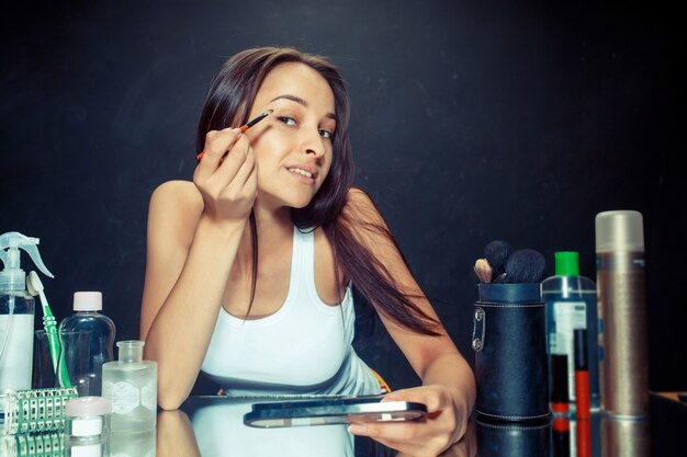 Beauty woman applying makeup. Beautiful girl looking in the mirror and applying cosmetic with a brush.