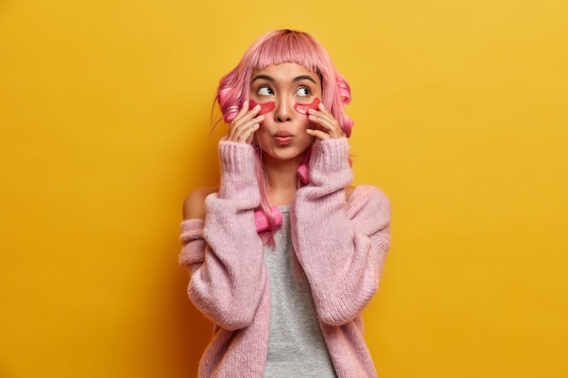 Free Photo beauty woman touches patches, looks wondered above, has surprised expression, wears hair curlers, dressed casually