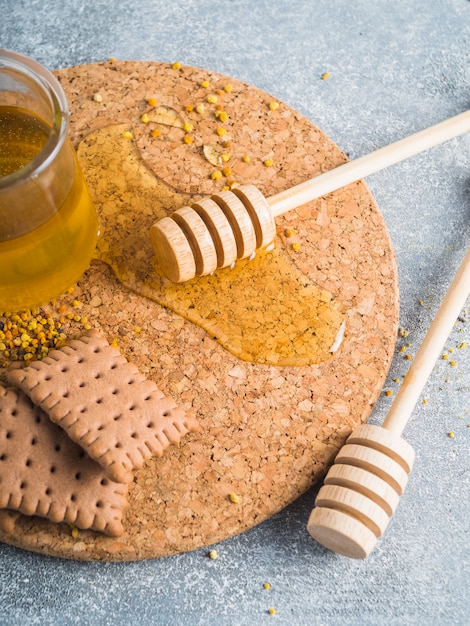 Free photo bee pollens; honey; biscuits and wooden dipper on cork coaster