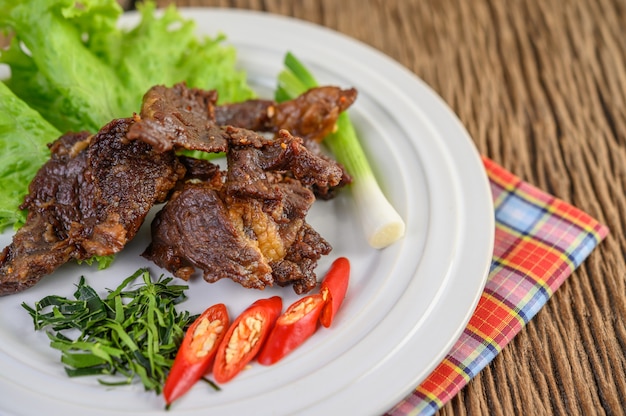 Free photo beef fried thai food on a white plate with spring onion, kaffir lime leaves, chilies, salad and chili paste in a cup.