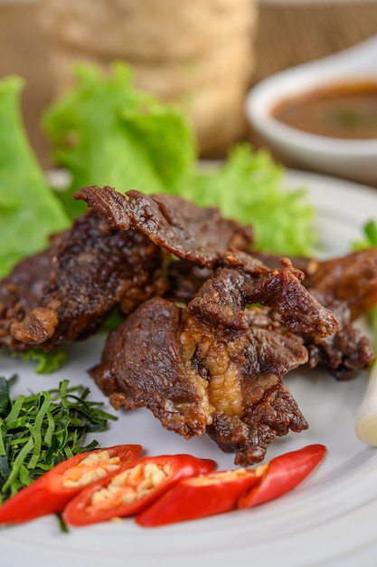 Free photo beef fried thai food on a white plate with spring onion, kaffir lime leaves, chilies, salad and chili paste in a cup.