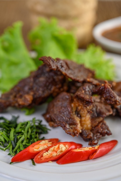 Free photo beef fried thai food on a white plate with spring onion, kaffir lime leaves, chilies, salad and chili paste in a cup.