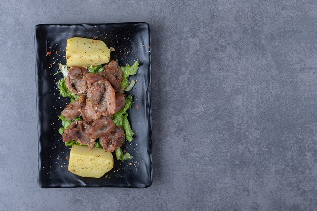 Beef kebab and boiled potatoes on black plate.