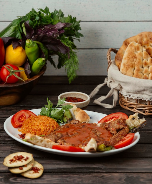 Beef kebab garnished with tomato slice, served with bulgur, bread and vegetables