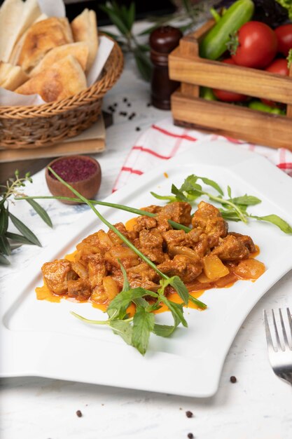 Beef meat slices stew in tomato sauce with onions and bell peppers. Served in white plate with basilic . 