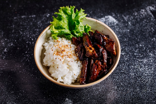 Beef steak with rice garnish and lettuce leaf inside white bowl.