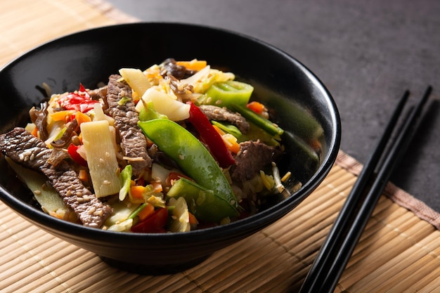 Beef, vegetables and sesame seeds in black bowl on black slate background