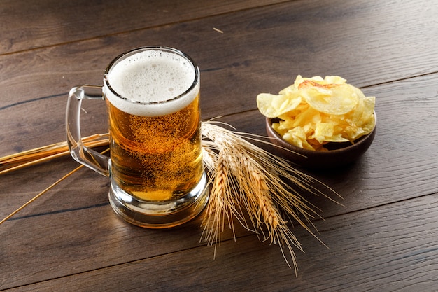 Beer with wheat ears, chips in a glass on wooden table, high angle view.