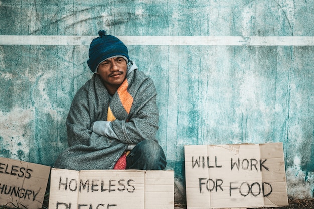 Free photo the beggars sat beside the street with a homeless message. please help and work with food.