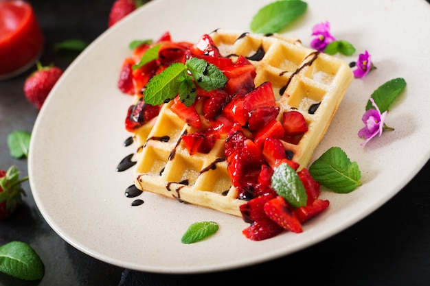 Belgium wafers with strawberries, chocolate and syrup on a plate.