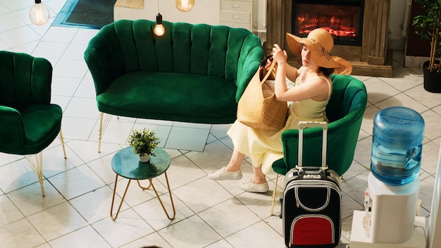 Free photo bellboy helping woman guest to carry baggage to her room, traveller with trolley bags waiting in lounge area. professional bellhop provising luxury service to hotel customers. handheld shot.