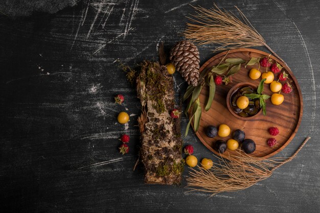 Free photo berry mix on a wooden platter with oak branches and cones aside in the middle