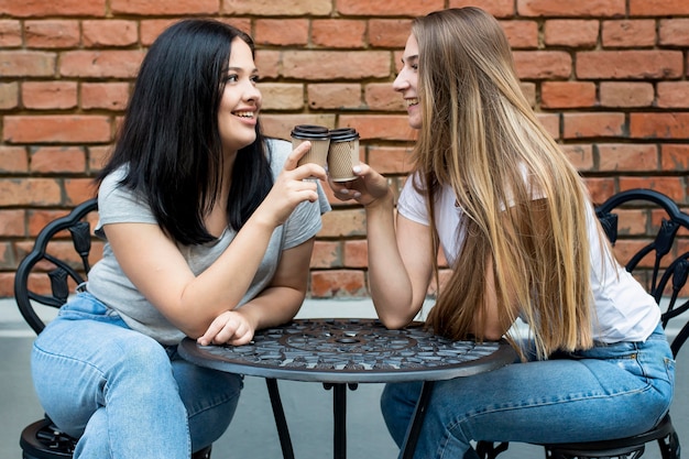 Best friends cheering with coffee glasses outside