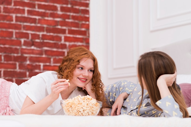 Free photo best friends eating popcorn while in bed