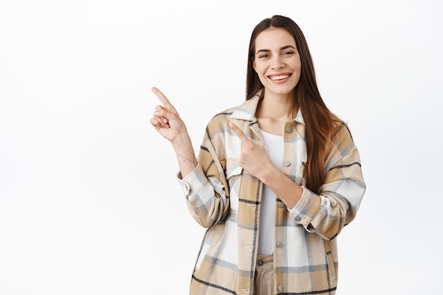 Free photo best offer on market smiling beautiful woman pointing fingers aside showing advertisement on left side copyspace display information standing over white background